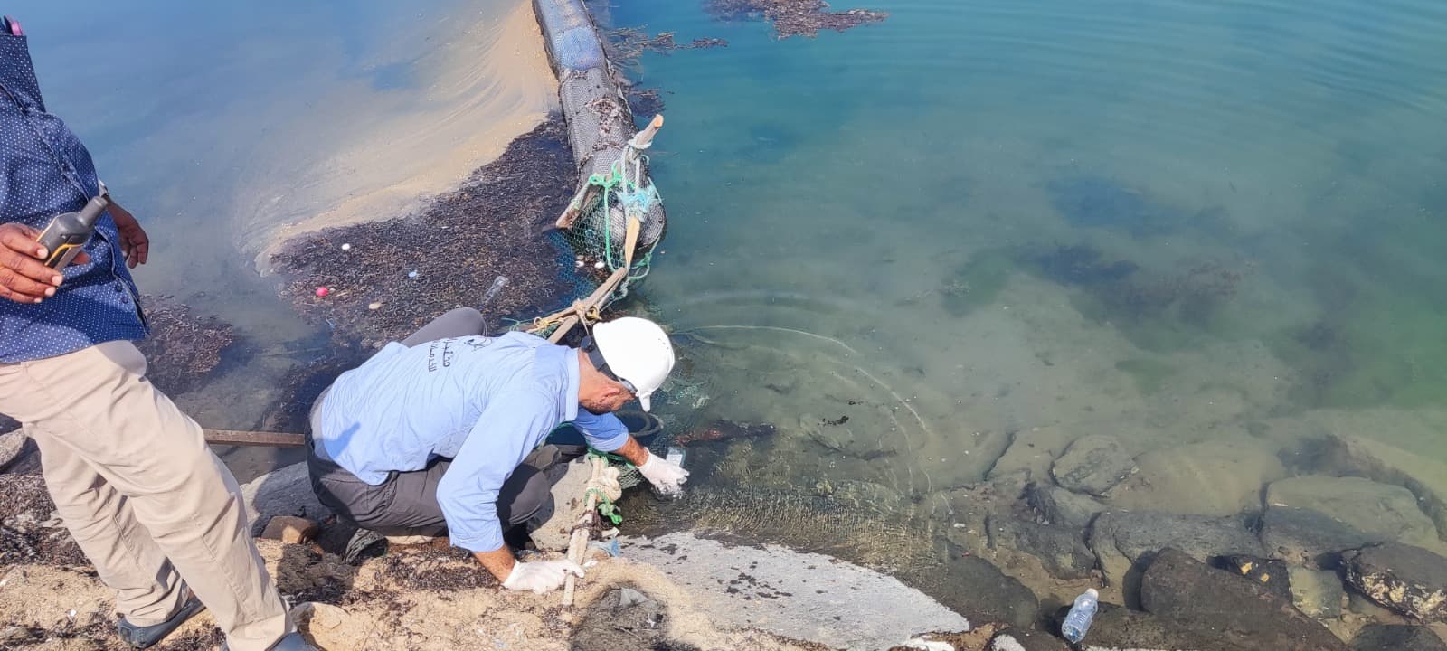 Technician collecting water samples at coastal monitoring site
